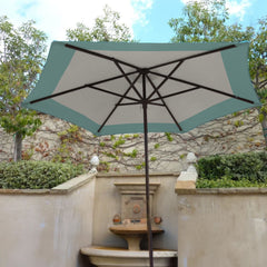 The 9ft Market Patio Umbrella 6 Rib Replacement Canopy Duet Light Blue by Formosa Covers, with its large rectangular shape and turquoise trim surrounding a beige center, is made from UV-treated fabric to provide shade in an outdoor patio area. The umbrella is supported by a dark metal pole. Behind it, a stone fountain stands against a wall adorned with climbing plants and greenery.