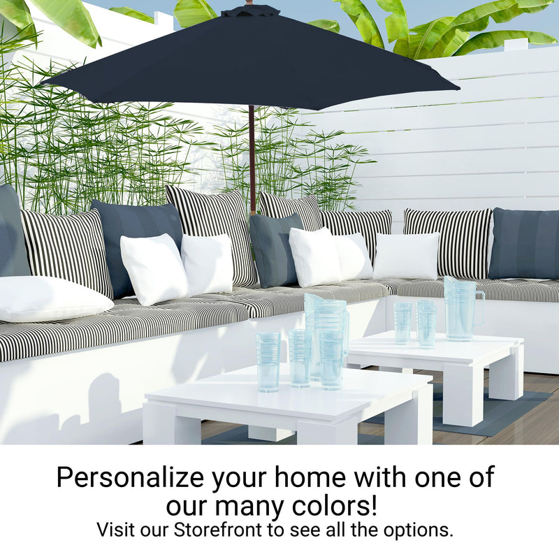 A modern outdoor patio setup featuring a cushioned L-shaped sofa adorned with striped and plain pillows, a large, durable 11ft Market Patio Umbrella with an 8 Rib Replacement Canopy in Dark Blue by Formosa Covers, and two white coffee tables with blue glassware on top. Lush green plants and a white fence provide a serene backdrop. Text reads: "Personalize your home with one of our many colors! Visit our Storefront to see all the options.