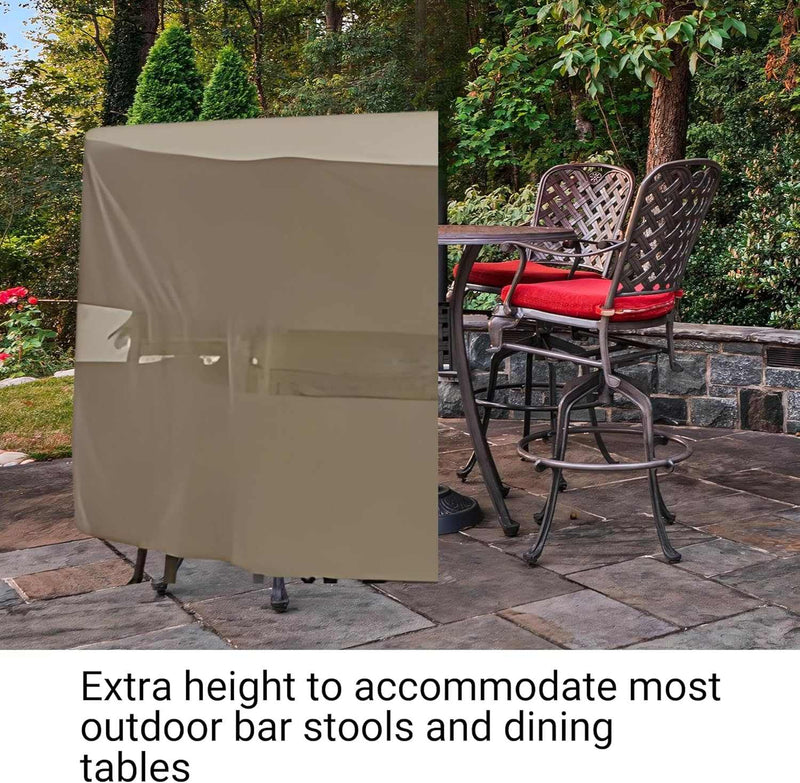 On a stone patio, a stylish setup features a covered table and two elevated bar stools with red cushions, embraced by lush greenery and bordered by a brick wall. The text highlights the "Patio Bar Height Dining Set Cover 98"Dia./L x 41"H Classic Taupe" from Formosa Covers, emphasizing its extra height suitable for most outdoor bar stools and dining tables, crafted from UV-treated polyester for enhanced water resistance.