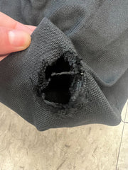 Close-up of a person's hand holding a piece of the Defective finial hole cut- 9ft Market Patio Umbrella 8 Rib Replacement Canopy Black Olefin from Formosa Covers, featuring a large, frayed hole. The worn and damaged material resembles an umbrella canopy. The background shows a textured, light-colored surface.