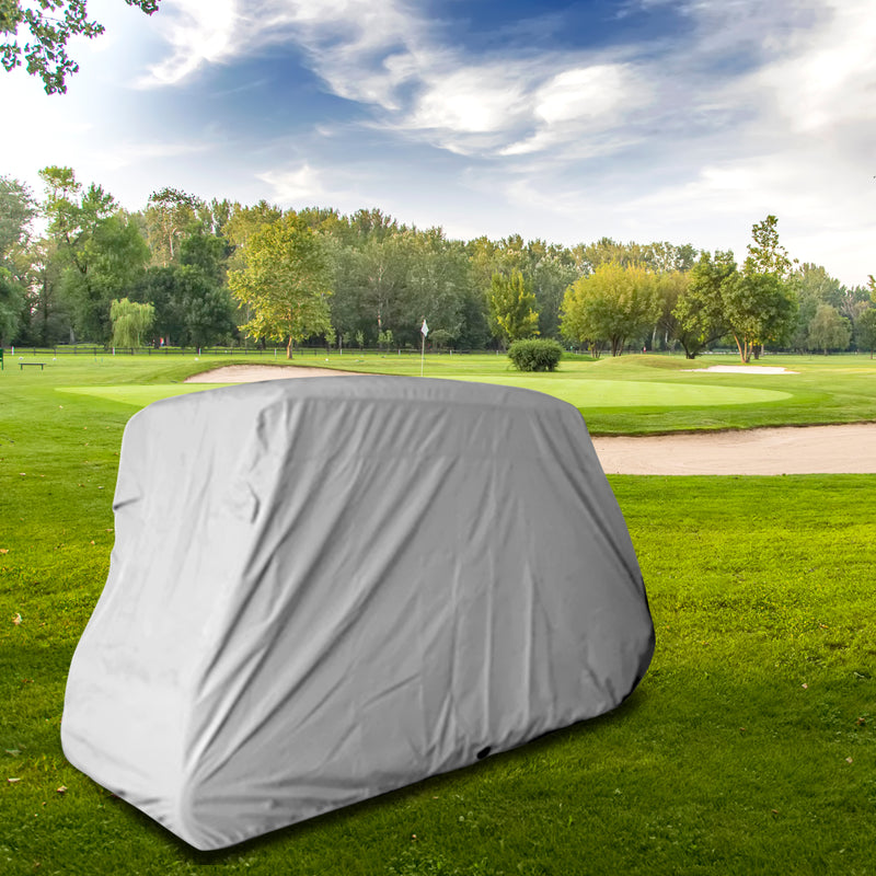 A 6 Passenger Golf Cart covered with a UV-treated, waterproof storage cover in gray from Formosa Covers is parked on the green grass of a golf course. The background features a lush area with several trees, a sand trap, and a flag marking one of the holes. The sky is partly cloudy, providing a serene atmosphere.